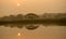 Morning sun with water reflection in a golden pond and silhouette view of big rain tree