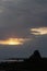 A morning sunrise peaks through heavy clouds to reveal a silhouette of a tufa at Mono Lake.