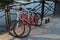 In the morning two bikes white and red of travelling together persons parked and locked with anti-theft cables to fence