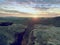 Morning view over crack sandstone edge into forest valley, daybreak Sun at horizon.