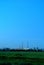 Morning view of a verdant field and pipes of a thermal power plant on the horizon.