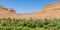 Moroccan clay village perched between orange mountains with palm tree oasis in front, Morocco, North Africa