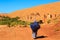 Moroccan woman carying a big bag with herbs with kasbah