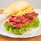 Mortadella sandwich, lettuce and cheese on a white plate and a bamboo mat with white background on a table with white towel,