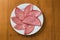 Mortadella slices served on a white plate, on a wooden background. top view