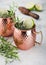 Moscow mule cocktail in a copper mug with lime and rosemary and wooden squeezer on ligh background