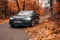 Moscow, Russia - 13 October 2019, black audi a6 driving in the forest. Deep autumn. A lot of orange fallen leaves.