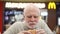 MOSCOW, RUSSIA- CIRCA JANUARY 2018: Hungry senior man eating hamburger at McDonald`s on food court