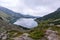 Mossy mountains in the Polish Tatras with a small turquoise lake and rocks in the middle of the mountain with white fog and clouds