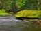 Mossy sandstone boulders in water of mountain river. Clear blurred water with reflections.