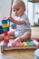 Mother With 8 Month Baby Son Learning Through Playing With Coloured Wooden Blocks At Home