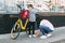 A mother adjusts her son`s sneakers before riding a bike to school. A boy wearing a mask and carrying a backpack is about to go t