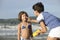 Mother applying sunscreen to daughter at beach.