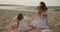 Mother and baby daughter sit on the beach near the sea playing together