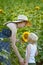 Mother and baby son stand and inhale the scent of sunflower on the background of a blooming field