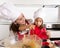 Mother baking with little daughter in apron and cook hat filling mold muffins with chocolate dough