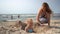 Mother in bikini bury her little blond girl in the beach sand. camera movement