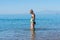 mother in black sunglasses and smiling baby boy son in green baseball cap playing in the sea in the day time. Positive human emot