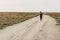 Mother carrying a baby on a sand path on a rural green plain landscape