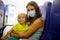 Mother and child, boy and mom, wearing masks and using disinfection, sitting in airplane
