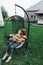 Mother and child ride on a wicker rattan cocoon swing. son shakes a woman, shakes a summer vacation in nature