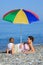 Mother with child under umbrella on pebble beach