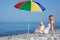 Mother with child under umbrella on pebble beach