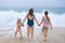Mother and children playing on the ocean beach. Family enjoying the ocean. Mother holds girls's hands and they all