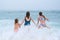 Mother and children playing on the ocean beach. Family enjoying the ocean. Mother holds girls& x27;s hands and they all
