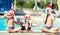 Mother with children in Santa hats celebrate the New Year in hot countries. The family eats strawberries and swims in the pool. N