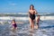 Mother and children on sea rest. Family are on sea beach. Mother, son and daughter in swimwear running on sea water. Woman with