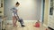 Mother clean dust from the floor with a vacuum cleaner and a little child`s daughter are playing near.