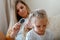 Mother combing daughter long hair by hairbrush. Caucasian blonde mom combing curly blond kid chaild. Mom does hair