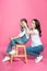 Mother covering eyes to cute smiling daughter sitting on stool