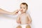 Mother creaming cute infant girl face. Little baby girl with cream on her face sitting on the white background