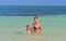 Mother and cute daughter playing and swimming in blue ocean.