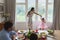 Mother dancing with her daughter while father and son sitting at dining table