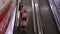 Mother with daugher in trolley riding escalator to next floor in shoping centre.