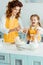 Mother and daughter adding smashed egg to flour in bowl while cooking together in kitchen