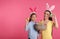 Mother and daughter in bunny ears headbands with Easter eggs on color background