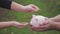 Mother and daughter child putting coins into piggy bank. Woman holds piggy bank while girl puts coins inside outdoor