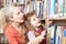 Mother And Daughter Choosing Book From Library Shelf