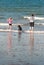 A mother and daughter with a dog jump over the breaking waves on a beach