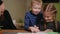 Mother and daughter doing a school homework assignment, a little boy watches it. Brother helps to do homework.