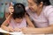 Mother and daughter drawing together with crayons. Adult woman helps girl study or draw together at home in living room. Happy