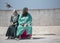 Mother and daughter, dressed in abaya and hijab, take a seat along the harbour front