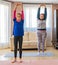 Mother and daughter dressed in sportswear exercising between white sofas in the living room at home