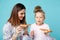 Mother and daughter eating pizza sitting on the floor in pajamas isolated over the blue background.