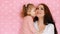 Mother and daughter embrace, smiles, have fun, laugh and kissed. Close-up portrait young woman and her child on pink