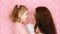 Mother and daughter embrace, smiles, have fun, laugh and kissed. Close-up portrait young woman and her child on pink